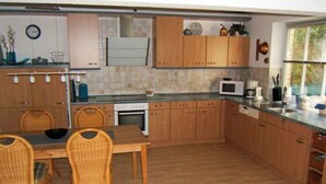 A kitchen with wooden cabinets, a dining table with chairs, a microwave, and a window with blinds. - Heinrich Tiarksstrasse 36 (Wangerland)