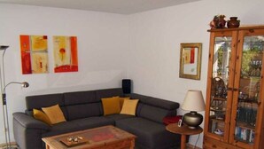 A living room with a dark grey sofa, wooden coffee table, and a cabinet with glass doors. - Heinrich Tiarksstrasse 36 (Wangerland)