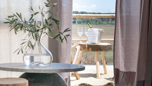 Ein Zimmer mit Blick auf ein Feld, ein Tisch mit einer Pflanzvase und ein kleiner Holzschemel mit Flasche und Gläsern.