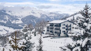 A modern multi-story building with balconies, surrounded by snow-covered trees and mountains. - Apartment With Infinity Pool (Sankt Martin am Tennengebirge)