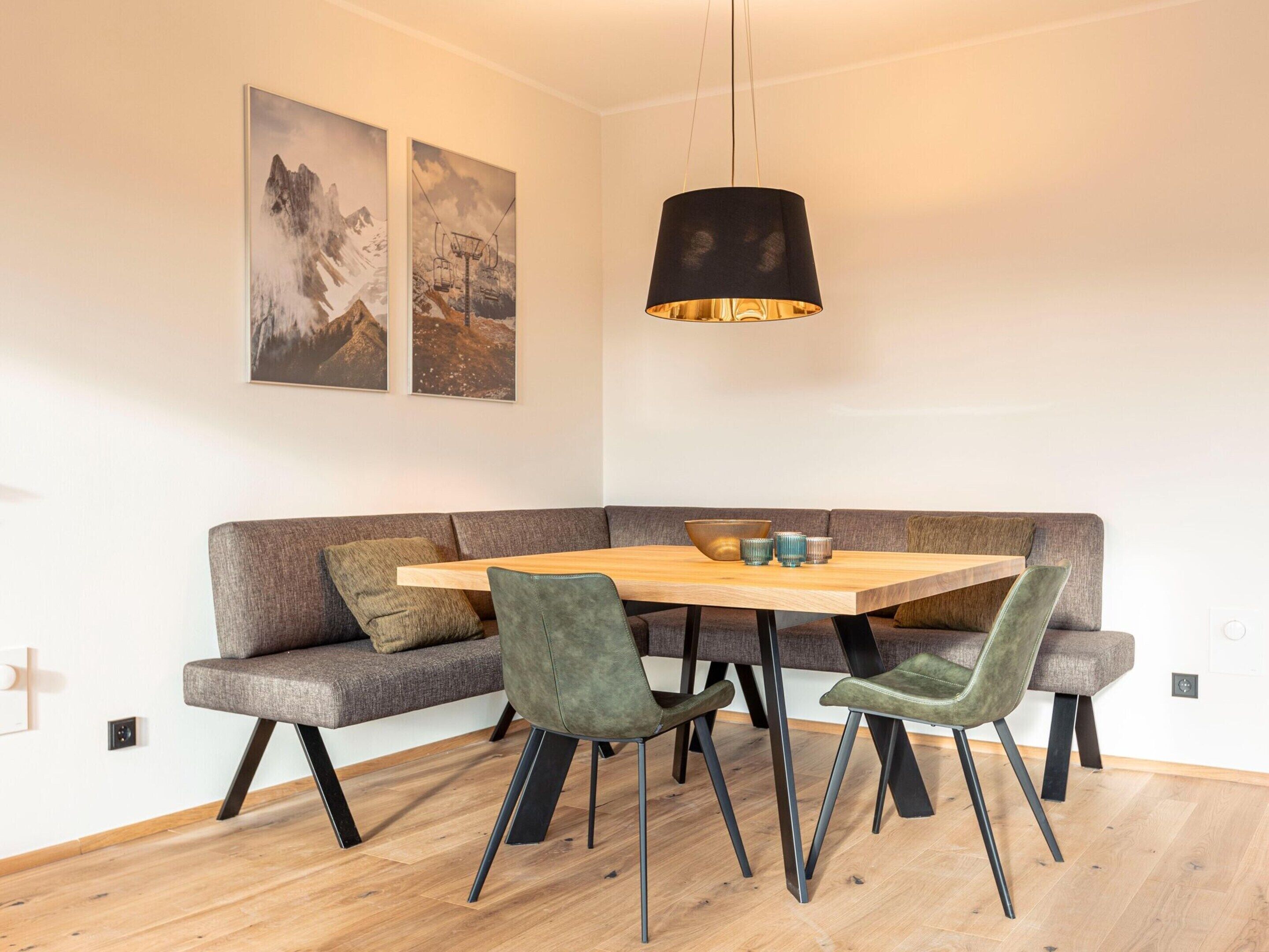 A modern dining area with a wooden table, green upholstered chairs, and a black pendant light.