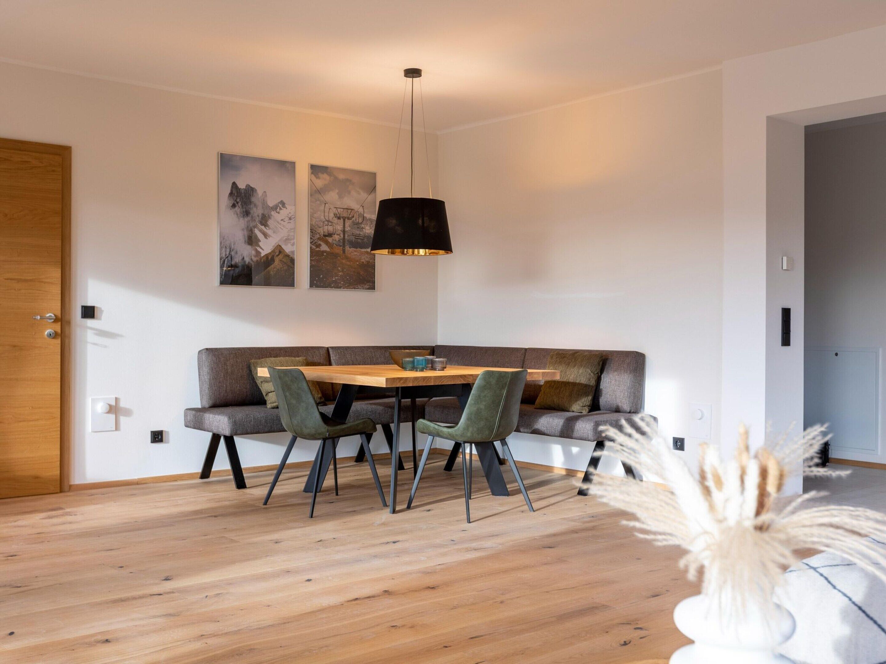 A modern dining area with a wooden table, green upholstered chairs, and a black pendant light.