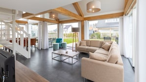 A spacious living area with a large sofa, a coffee table, and a TV. There is a staircase with a railing leading to another level. - Holiday Home in Renesse Near the Beach (Renesse)