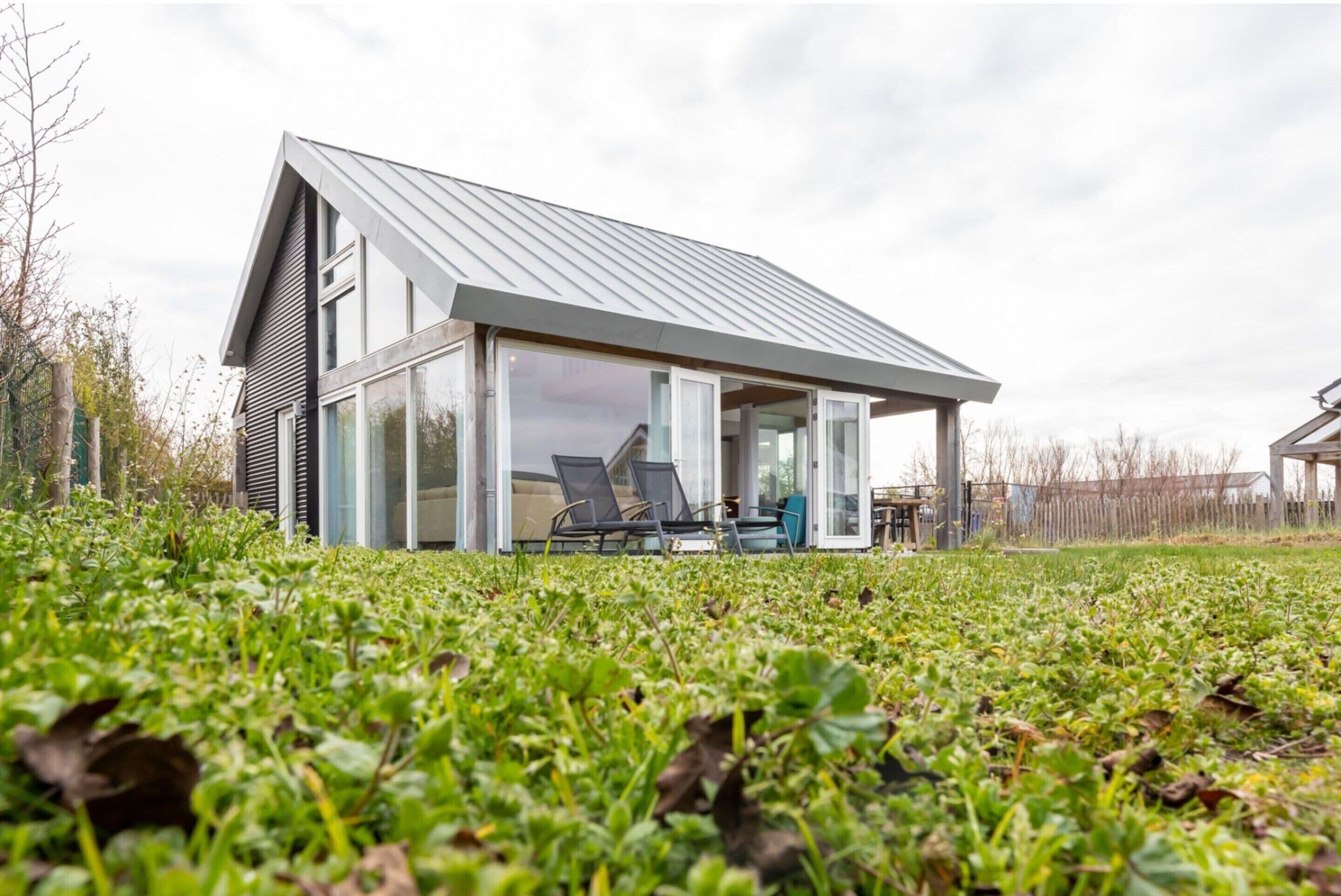 Een modern huis met een schuin dak, grote glasramen en een terras met tuinmeubilair.