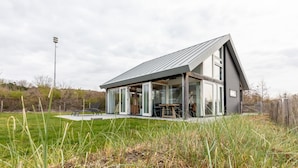 A modern house with a large glass facade, a sloped roof, and a patio area with outdoor furniture. - Holiday Home in Renesse Near the Beach (Renesse)