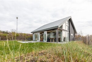 A modern house with a large glass facade, a sloped roof, and a patio area with outdoor furniture.