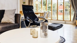 A modern living room with a black leather chair, a white round table with two glass candle holders, and a view of the outdoors through large windows. - 5 Person Holiday Home in Gedser (Gedser)