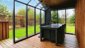 A covered patio with a table and chairs, large glass windows, and a wooden deck. - 5 Person Holiday Home in Gedser (Gedser)