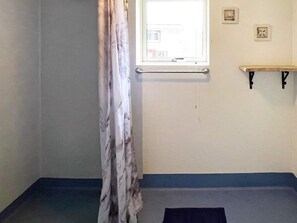 Een kamer met raam, gordijn, plank en bed.