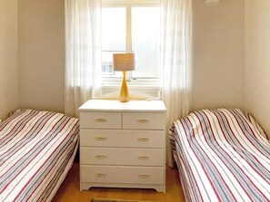 Een slaapkamer met twee bedden, een dressoir met lades, een lamp en een raam met gordijnen.
