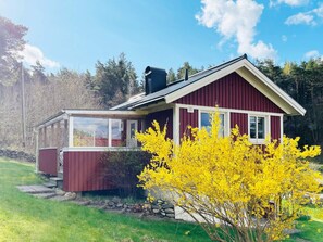 Ett rött trähus med ett glashus och ett gult, blommande träd i förgrunden.