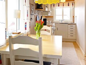 Eine kleine Küche mit weißen Schränken, einem Holztisch und einem Fenster mit Vorhängen.
