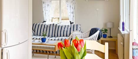 A compact living space with a kitchenette, a sofa, a dining table, and a window with curtains.