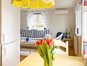 Een functionele leefruimte met een kitchenette, een bank, een eettafel en een raam met gordijnen.