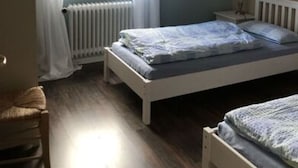 Une chambre avec un plafond en pente, un lit avec un cadre blanc, une table de chevet, un radiateur et une fenêtre avec des rideaux blancs.