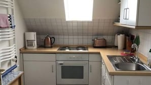 Une cuisine de taille réduite, équipée d’une cuisinière à gaz, d’un four et d’un petit évier. Une fenêtre se trouve au-dessus de l’évier et le sol est en bois.