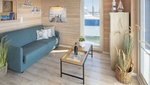 Interior acogedor de una cabaña con un sofá azul, una mesa de centro de madera y un ventanal con vistas a barcos.