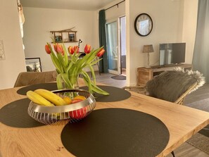 Uma mesa de jantar com uma fruteira, um vaso com tulipas e um relógio na parede.