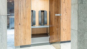 Un ascenseur moderne avec des panneaux en bois et une porte en verre, qui donne sur une pièce où se trouvent un banc et une petite table.