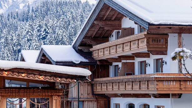 Un chalet traditionnel en bois, doté d’un balcon, qui se dresse sur fond de montagnes enneigées.