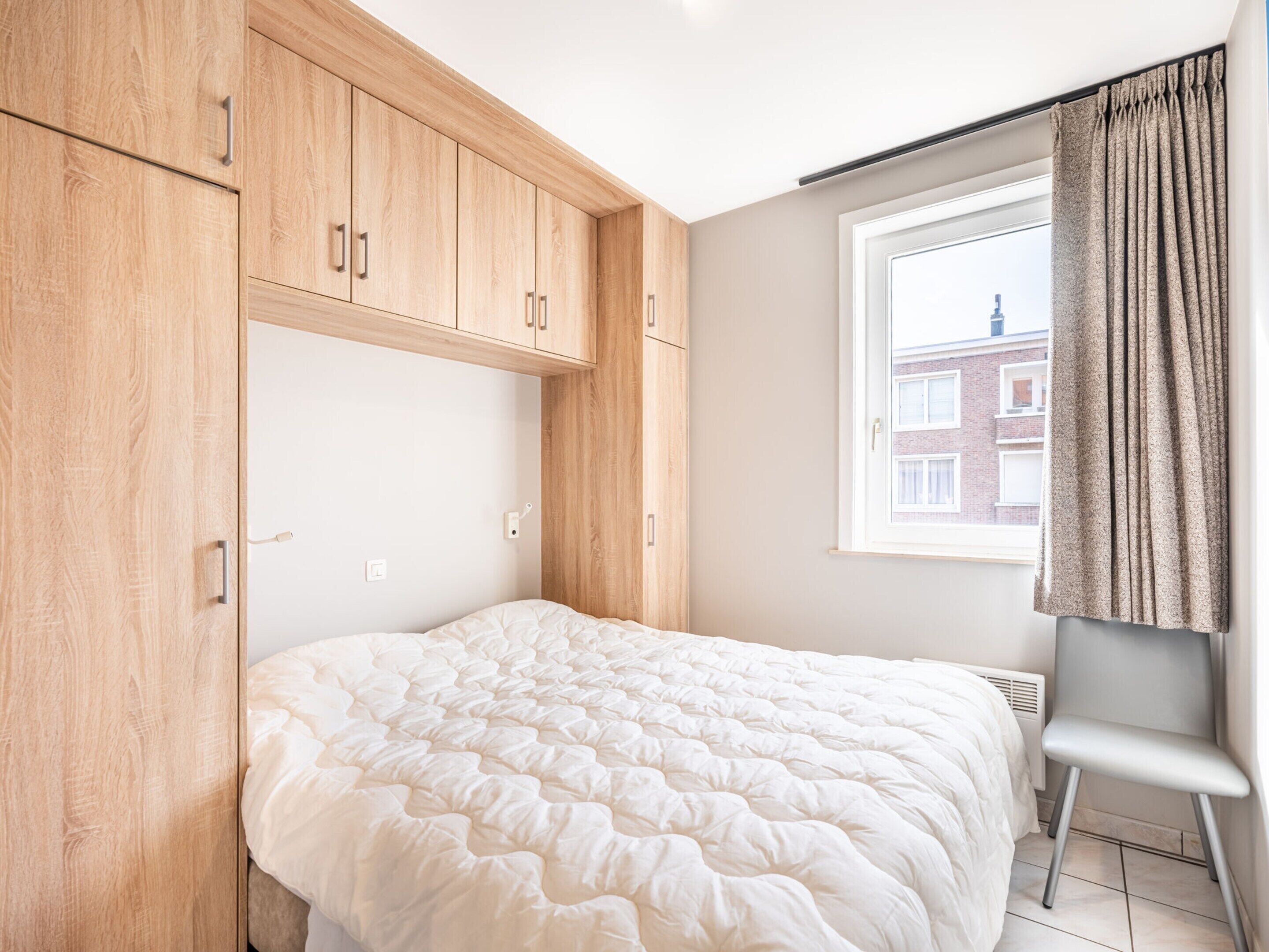 A bedroom with a bed, wooden wardrobe, and a window with curtains.