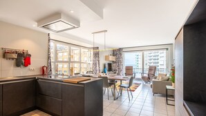 A modern kitchen with a central island, large windows, and a dining area with a view of the city. - Apartment in Koksijde With Sea View (Koksijde)