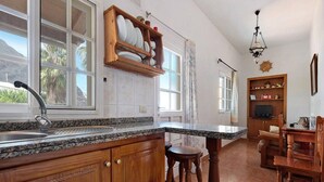 A kitchen with wooden cabinets, a granite countertop, a built-in shelf with dishes, a dining area with a wooden table and chairs, and a chandelier. - Country House Buenavista Near Sea Beach (Buenavista del Norte)
