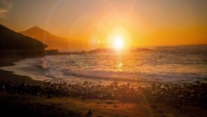 A sunset over a beach with waves, mountains in the background, and a crowd of people on the shore. - Country House Buenavista Near Sea Beach (Buenavista del Norte)