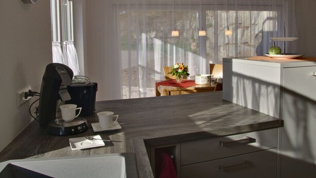 A modern kitchen with a coffee machine, a dining table with a vase of flowers, and a view of the outdoors through sheer curtains. - Rebenrain Comfortable Holiday Residence (Steinach)