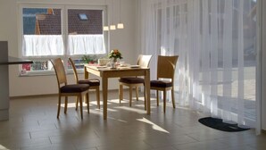 A dining area with a table and chairs, a window with curtains, and a view of buildings outside. - Rebenrain Comfortable Holiday Residence (Steinach)