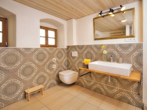 A bathroom with a white sink, a toilet, a wooden bench, a mirror with lights, and patterned tiles. - Oberprill Modern Retreat (Loitzendorf)
