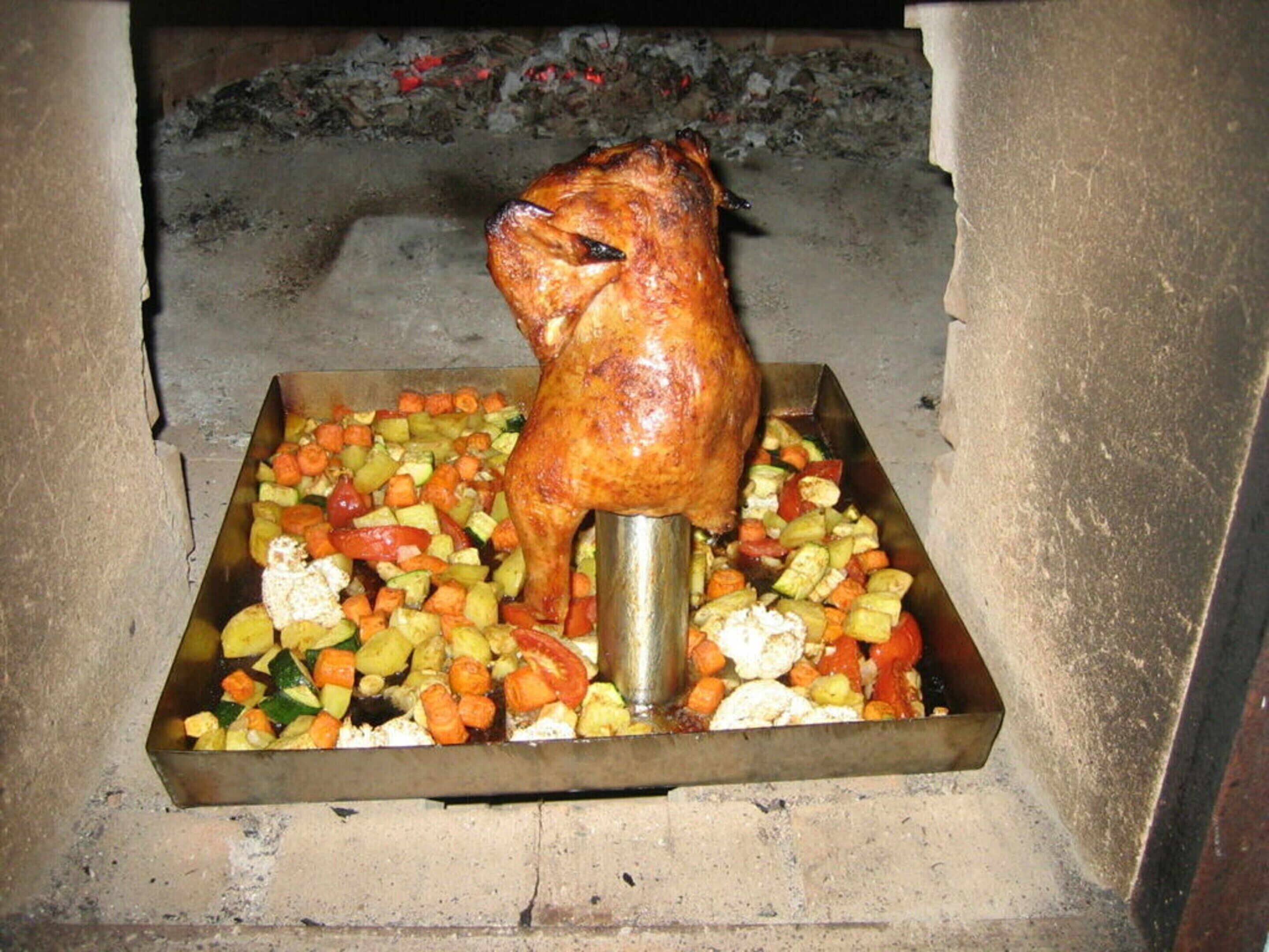 A roasted chicken on a spit with a tray of vegetables underneath.