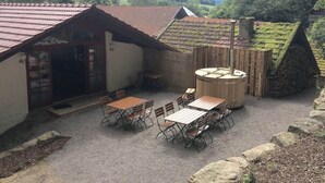 A rustic outdoor seating area with wooden tables and chairs, a stone well, and a wooden fence. - Oberprill Modern Retreat (Loitzendorf)