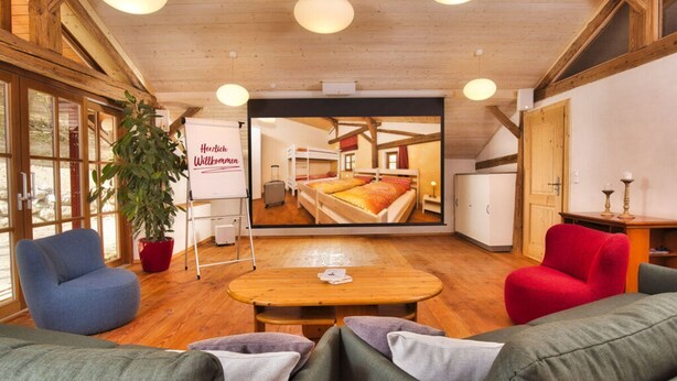 A cozy room with a large window, a wooden ceiling, a whiteboard with "Herzlich Willkommen" text, a plant, and a red chair. - Oberprill Modern Retreat (Loitzendorf)