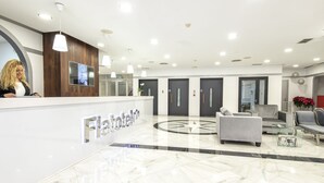 Un área de recepción moderna con suelo de mármol, mostrador de recepción y zona de estar con una mesa de centro.