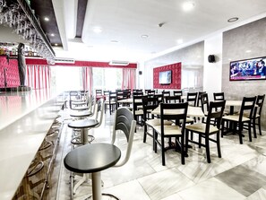 Een restaurant met een bar, verschillende tafels en stoelen, en een televisiescherm aan de muur.