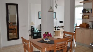 Un comedor con mesa y sillas de madera, un espejo en la pared y una zona de cocina con armarios y estantes.