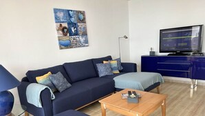 Una sala de estar moderna con un sofá azul oscuro, una mesa de centro de madera y un televisor sobre un mueble bajo.