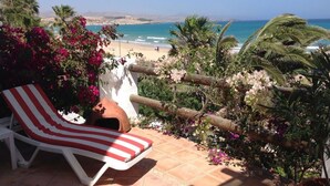 Una tumbona con funda a rayas rojas y blancas, una maceta de barro y vistas a la playa y al océano.