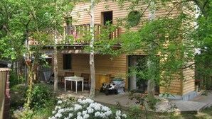 A two-story wooden house with a balcony, a small patio area with a table and chairs, and a garden with white flowers. - Nice Apartment in Lubmin (Lubmin)