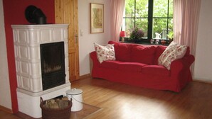 A living room with a fireplace, a red sofa, and a window with curtains. - Nice Apartment in Lubmin (Lubmin)