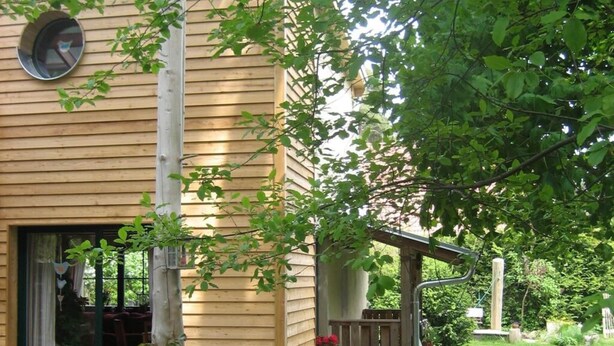 A wooden house with a covered porch, a visible window, and a garden area with a fence. - Nice Apartment in Lubmin (Lubmin)