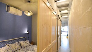 Quarto de hotel com cama, armário de madeira e corredor que leva a um banheiro.
