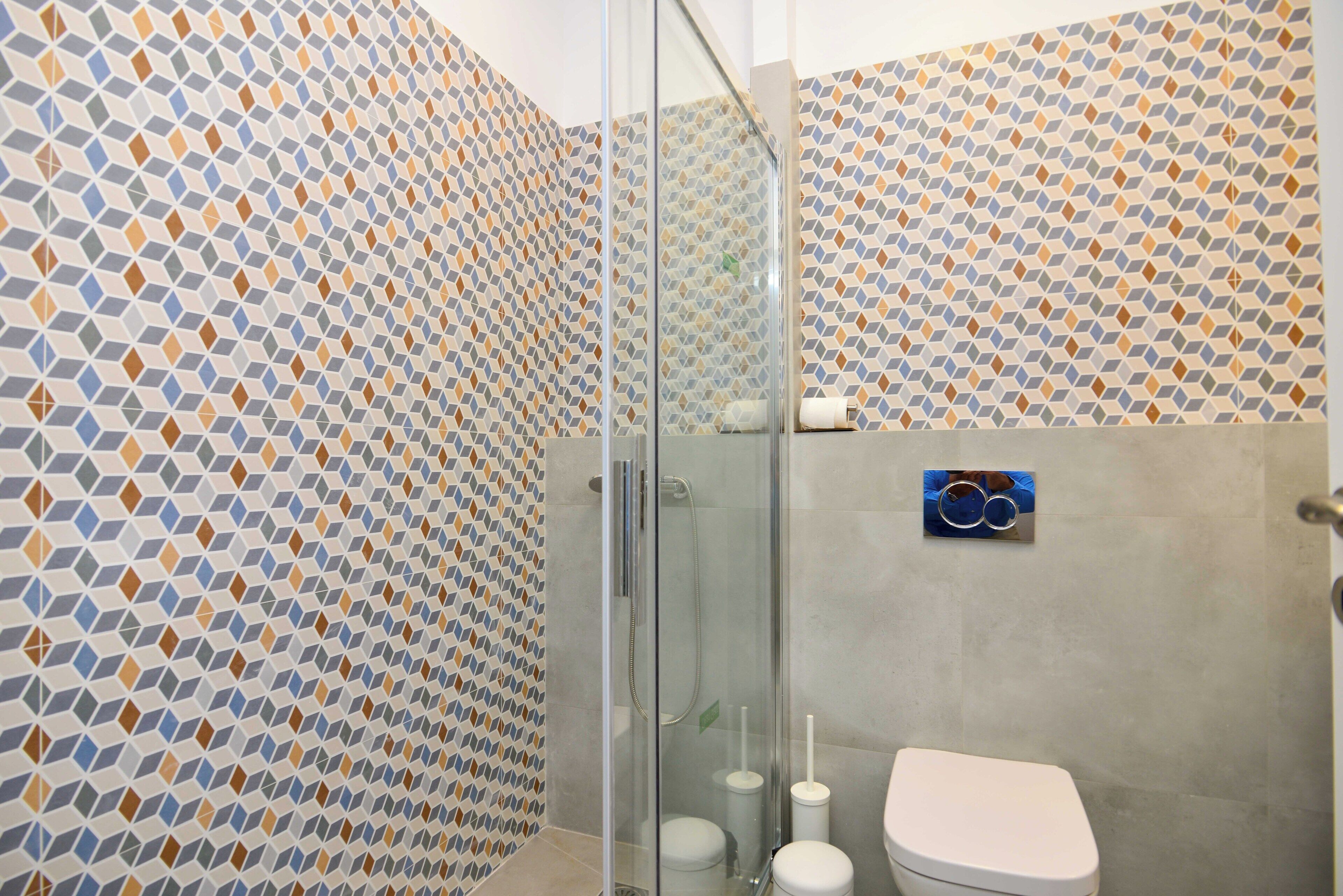 Een badkamer met een wand met een geometrisch patroon, een glazen douchecabine en een wit toilet.