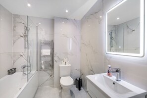 A modern bathroom with a glass-enclosed shower, a white toilet, a sink, and a marble-tiled wall. - Modern 1 Bedroom Apartment - Camberley (Camberley)