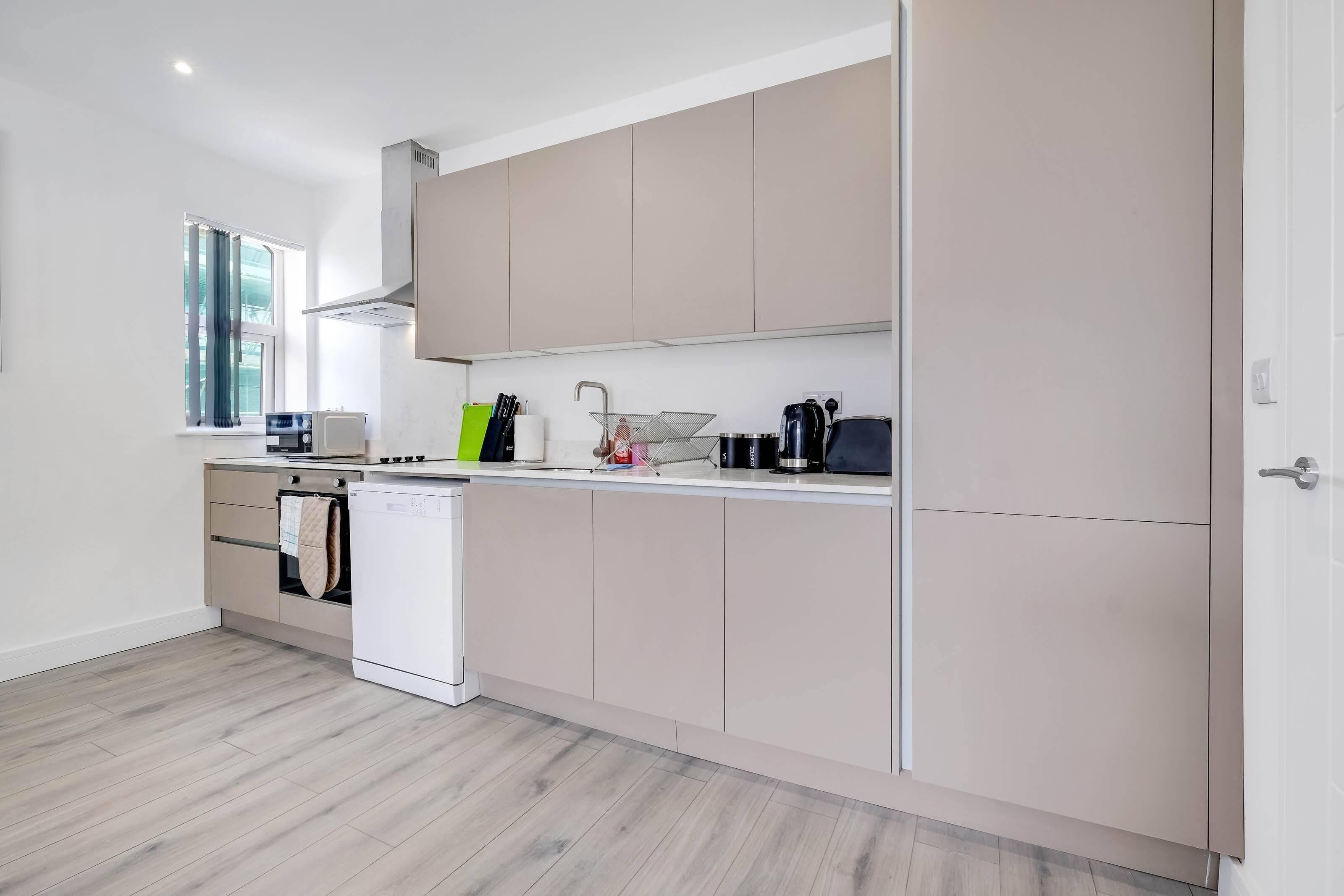 A modern kitchen with light wood flooring, white cabinets, a built-in oven, and a window with curtains.