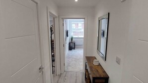 A hallway with a wooden bench, a mirror, and a door leading to a room with a window. - Modern 1 Bedroom Apartment - Camberley (Camberley)
