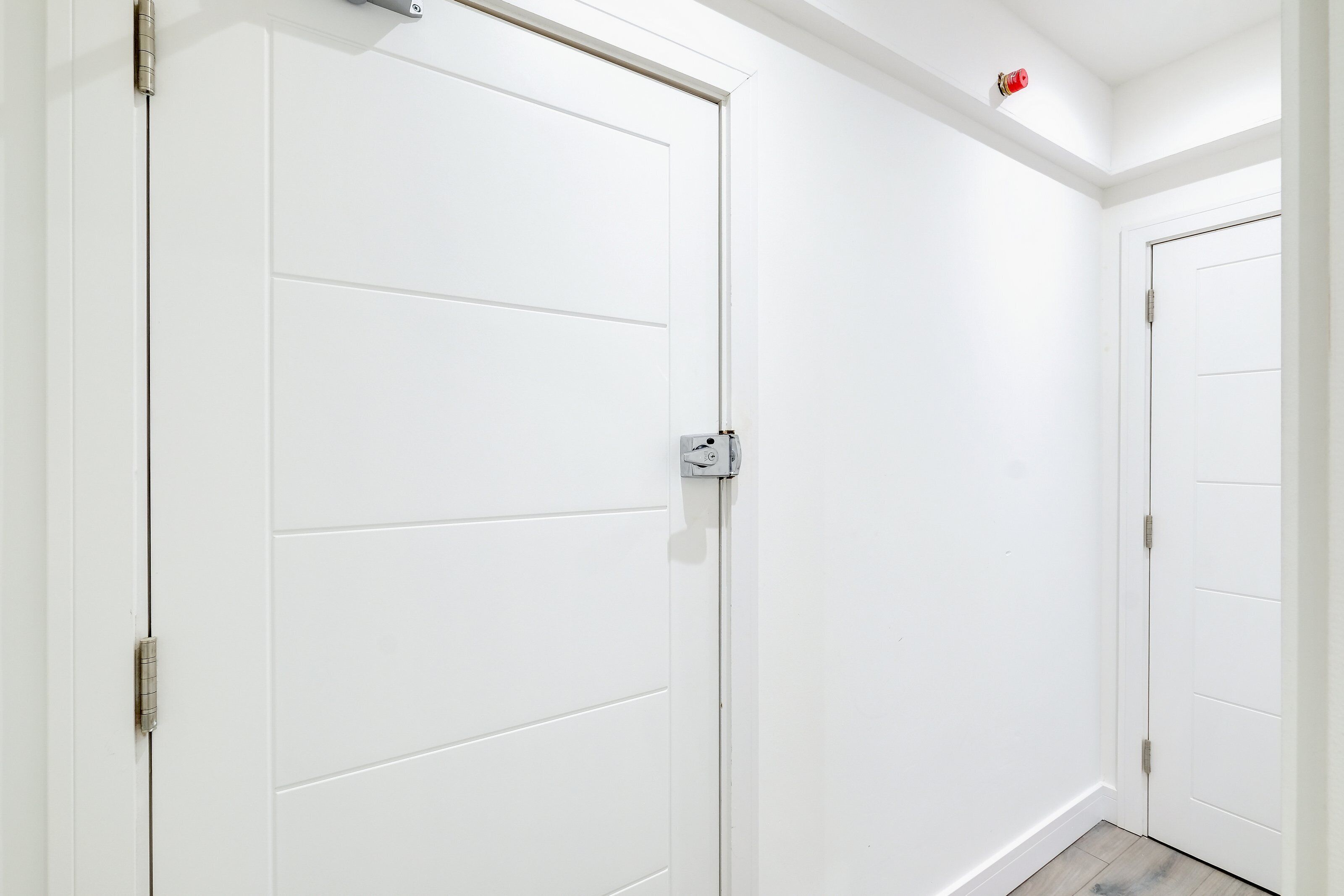 A white door with a metal handle and a small red object on the wall above it.