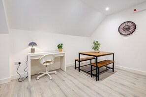 A modern room with a white desk, a white office chair, a small wooden table with a bench, and a potted plant. - Modern 1 Bedroom Apartment - Camberley (Camberley)