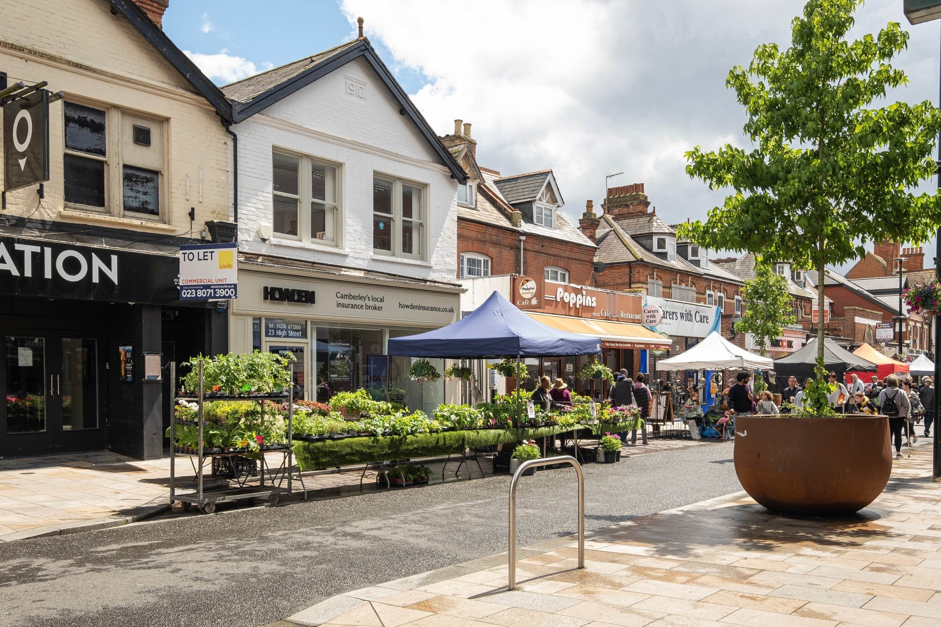 Une rue bordée de boutiques, un marché aux fleurs et un grand bac à fleurs.